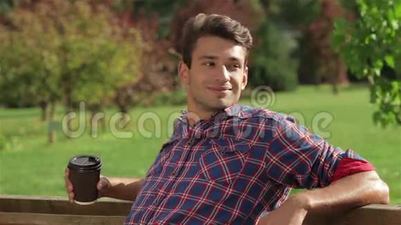在公园的长椅上喝咖啡的男人视频的预览图