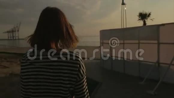 在日落或日出时美丽的年轻女子走在船上或码头上视频的预览图
