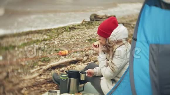 河岸上的旅游帐篷两个女孩坐在帐篷附近吃喝看着河视频的预览图