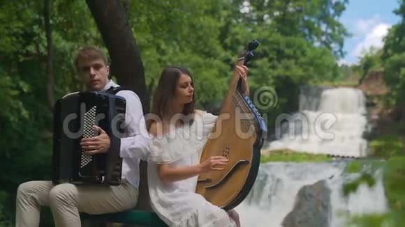 两位音乐家钢琴家和乐队演奏家在瀑布的岩石上演奏视频的预览图