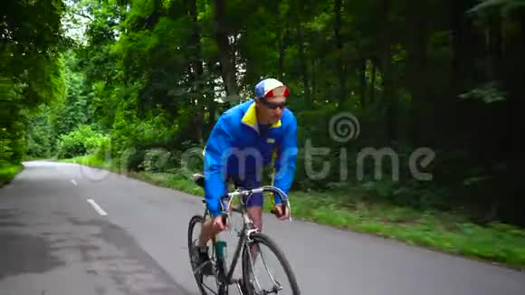 一个中年男子正骑着一辆公路自行车沿着一条森林的行驶视频的预览图