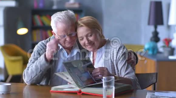 一对幸福的老人看着旧相册微笑着视频的预览图