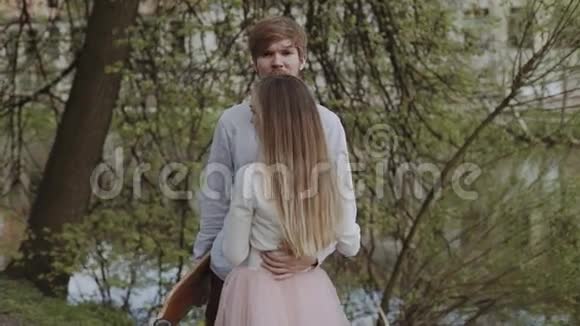 恋爱中的年轻夫妇牵着手在夏季公园散步穿着粉红色图塔裙的女人手里拿着长板视频的预览图