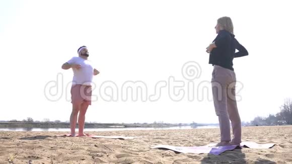 一个白种人的男人和一个女人在自然的河岸上练习动态瑜伽冥想技巧摆脱了视频的预览图