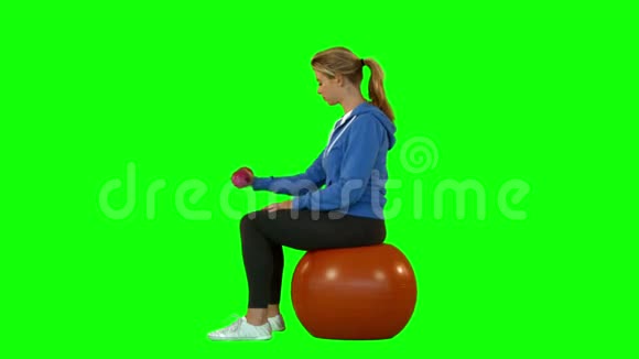健身女用哑铃坐在健身球上侧视图视频的预览图