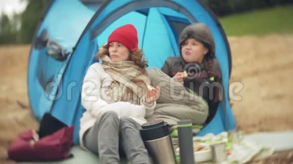 河岸上的旅游帐篷两个女孩坐在帐篷附近吃喝看着河视频的预览图