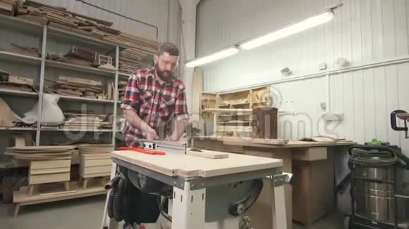 一个有胡子的木匠穿着衬衫车间里的木头上有一把圆锯视频的预览图