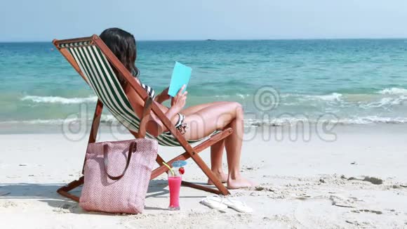 一个漂亮的黑发女人在甲板椅上看书视频的预览图