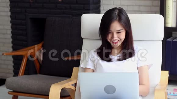 美丽的肖像亚洲年轻女子微笑着坐在沙发上在网上工作视频的预览图