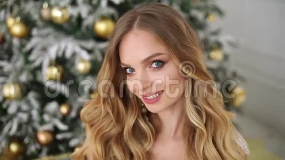一幅美丽的笑脸女人的画像她的发型和化妆把她可爱的婴儿抱在装饰好的圣诞树上视频的预览图