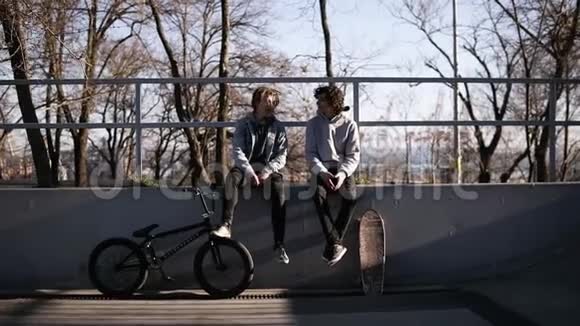 两个朋友的前视图滑板运动员和bmx骑手一起坐在城市滑板公园的高栏杆上视频的预览图
