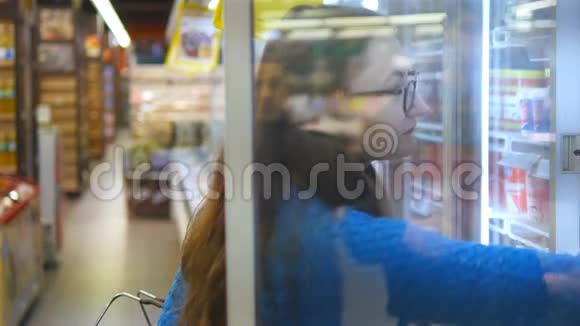带着购物车在冷藏区的超市里买奶制品或冷藏食品的年轻女子视频的预览图
