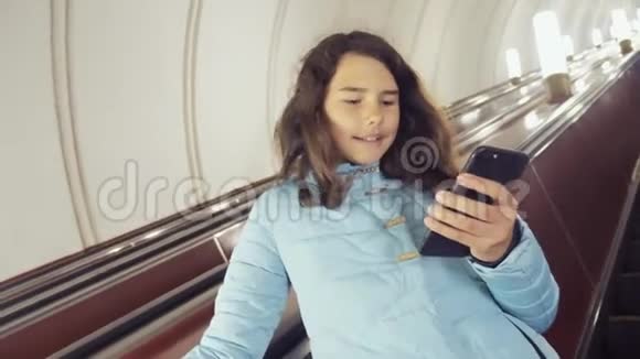 少女在地下地铁乘坐自动扶梯生活方式持有智能手机小女孩黑发女儿视频的预览图
