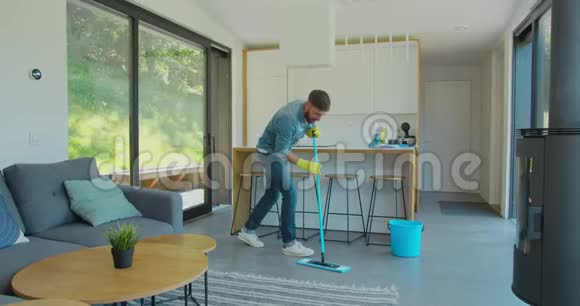一个戴着防护手套的男人在年底的时候用拖把唱歌跳舞在客厅打扫房子视频的预览图