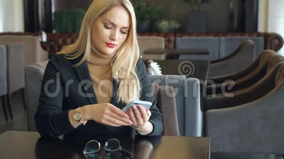 一位西装革履拿着电话的女商人坐在咖啡馆的桌子旁视频的预览图