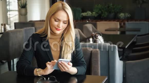 一位西装革履拿着电话的女商人坐在咖啡馆的桌子旁视频的预览图