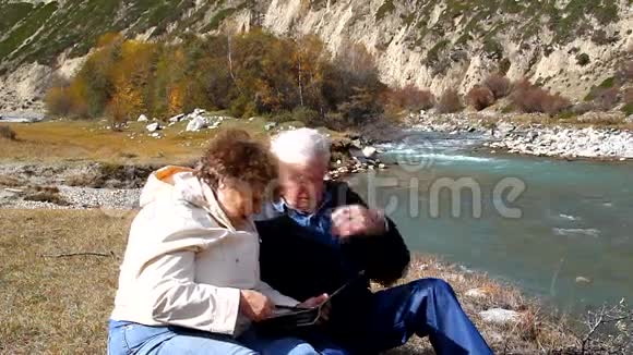 幸福的老夫妇坐在河岸上视频的预览图