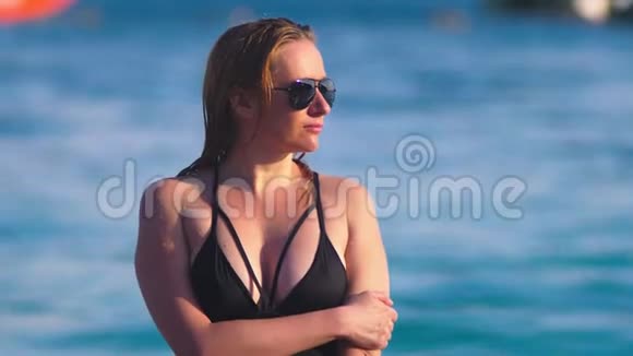 穿着黑色泳衣的金发女孩和白色沙滩上的黑色太阳镜有日光浴的漂亮模特视频的预览图