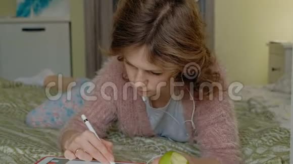 快乐的女孩听音乐用手写笔在家里的卧室里用平板电脑画画网上冲浪远程工作视频的预览图