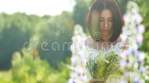 快乐的女孩在一个有花的田野里女孩在田野里微笑的女人拿着一束花在户外视频的预览图