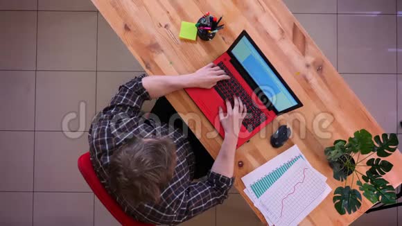 一位年轻的高加索商人在办公室的办公桌上用笔记本电脑打字的特写镜头视频的预览图