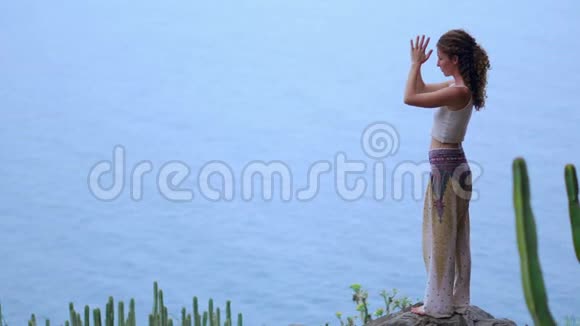 日落时在岩石海岸做瑜伽的年轻女子健康生活方式的概念和谐人性与自然这就是视频的预览图