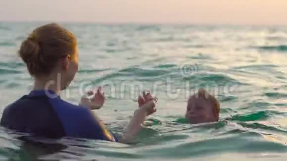 女子游泳教练教小男孩在日光浴时在海里游泳视频的预览图