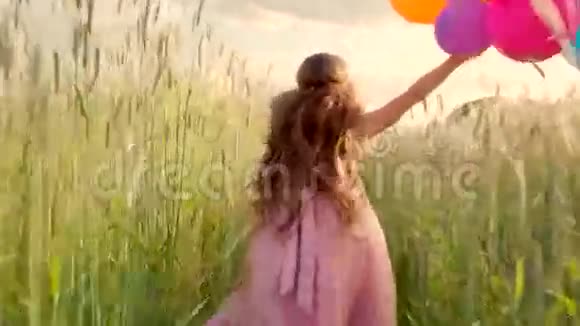 日落时分一个女孩带着彩色气球穿过麦田视频的预览图