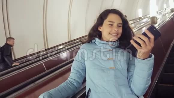 十几岁的女孩在地下地铁乘坐自动扶梯持有智能手机小女孩黑发女儿视频的预览图