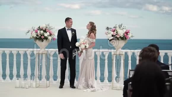 婚礼上的新娘和新郎一对相爱的年轻夫妇站在拱门前海边的婚礼视频的预览图