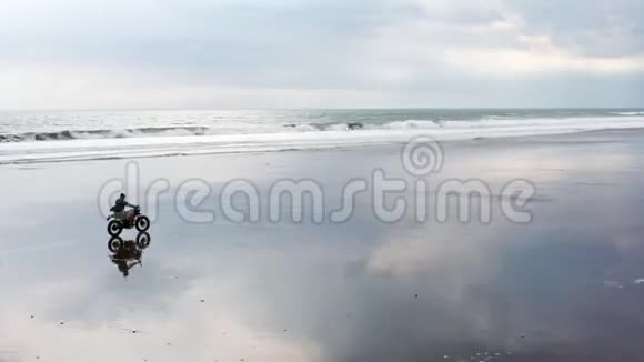 年轻英俊的嬉皮士骑着现代定制摩托车赛车在黑沙滩附近的水冲浪场地视频的预览图