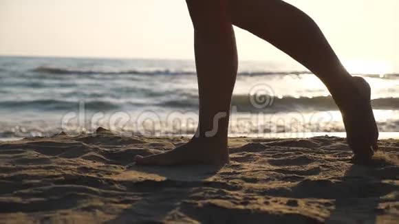 靠近女性的脚在沙滩上金色的沙滩上行走背景是海浪年轻女子的腿视频的预览图