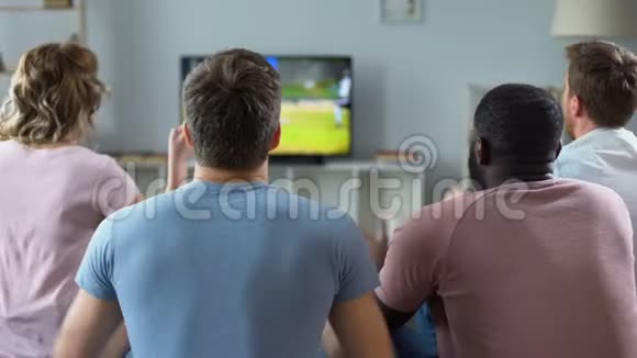 一群多民族的朋友为足球队加油在电视上观看比赛视频的预览图