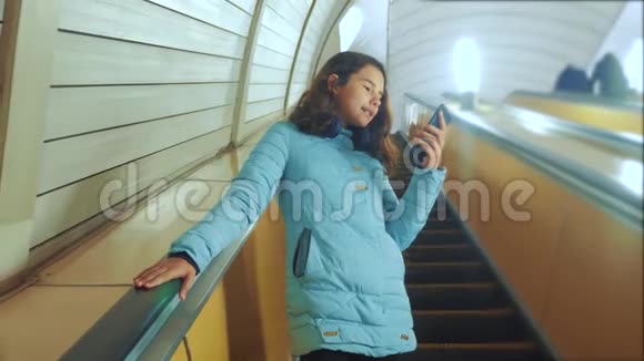 少女生活方式在地下地铁乘坐自动扶梯手持智能手机小女孩黑发女儿视频的预览图
