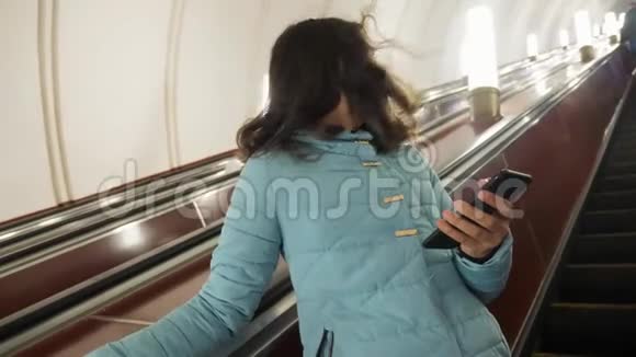 少女在地下地铁乘坐自动扶梯手持智能手机小女孩黑发生活方式女儿视频的预览图