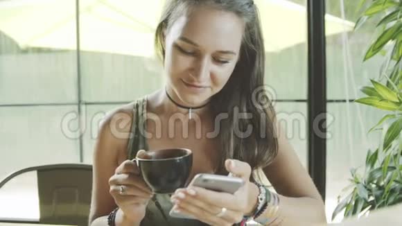 女性使用应用程序在电话微笑和喝咖啡在咖啡馆视频的预览图
