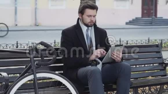 商人用平板电脑坐在靠近自行车的长凳上视频的预览图