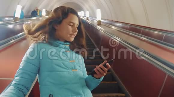 少女在地下地铁乘坐自动扶梯手持智能手机小女孩棕发女儿搜索视频的预览图