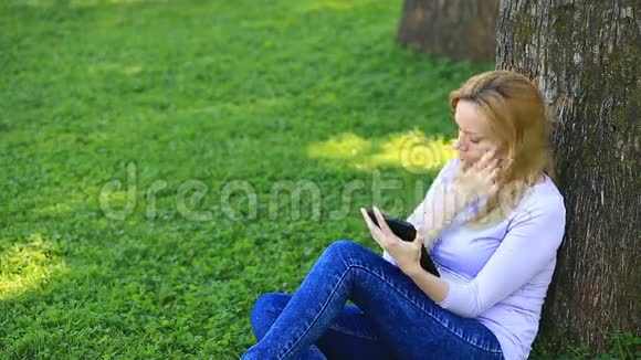 英俊的女人坐在棕榈树下用智能手机上网视频的预览图
