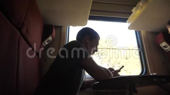男人的身影坐在火车车厢里坐在窗边坐着一辆智能手机铁路喝酒视频的预览图