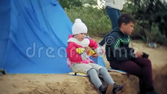 一个美丽的女孩和她的家人在一个旅游帐篷附近的河岸上的四弦琴上玩耍视频的预览图
