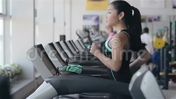 漂亮的亚洲女孩在健身房的跑步机上跑步左侧面照片视频的预览图
