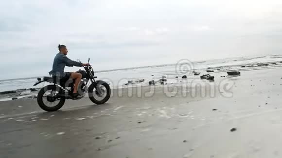 在海滩上骑摩托车的人巴厘岛海滩日落上的老式摩托车年轻的时髦男性享受自由视频的预览图