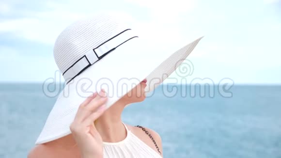 一位身穿白色宽边帽子和太阳镜的优雅女士欣赏海景4k慢镜头视频的预览图