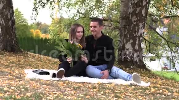 一对年轻夫妇坐在秋天公园的白色床单上视频的预览图