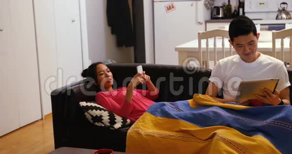 一对夫妇在客厅里用数码平板电脑和手机在沙发上放松视频的预览图