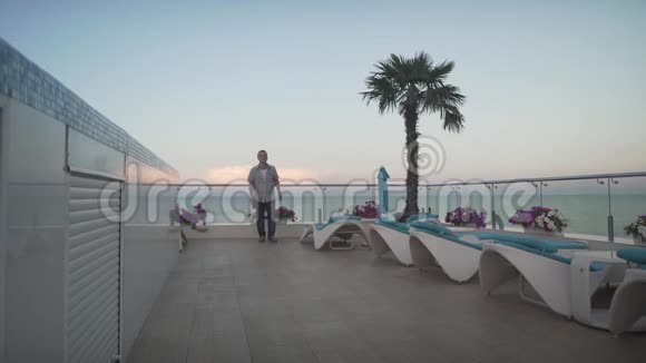 穿着休闲服装的男人穿着格子衬衫在美丽的傍晚夕阳西下阳台上在美丽的日落海景视频的预览图