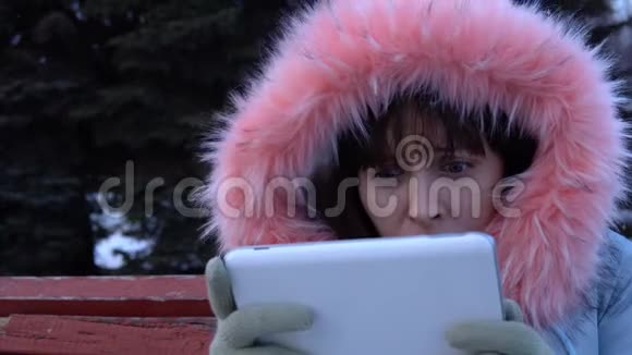 冬天一个穿暖和夹克的年轻女子在公园里使用数字平板电脑视频的预览图