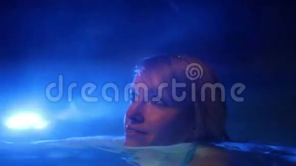 穿着蓝色比基尼的年轻女子晚上喜欢在室外游泳池游泳视频的预览图