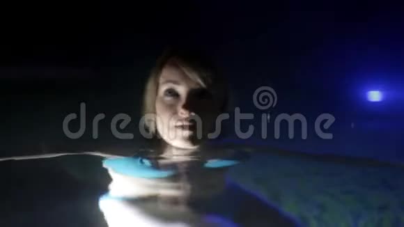 穿着蓝色比基尼的年轻女人晚上喜欢在户外游泳池里视频的预览图